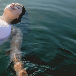 woman with dark hair floats in water with her eyes closed