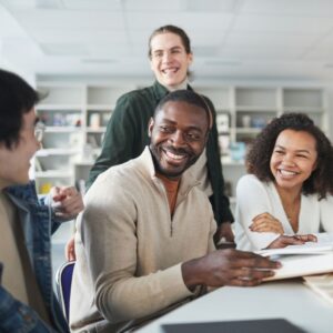 group of 4 people sit and stand around table with books on it